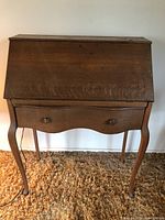 Full front view of the vintage wooden secretary desk showing the closed hinged writing surface and the single drawer below with wooden knobs.