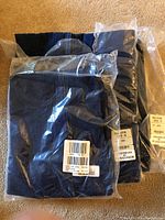 Three individually packaged dark blue denim skirts for women lying on carpet, sizes 14 and 16.