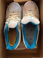 Top-down view of pair of white New Balance women's sneakers with blue interior lining in original box.