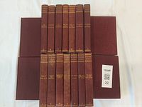 Top view of 18 leather bound books stacked and arranged, showing uniform binding color and gilded edges.