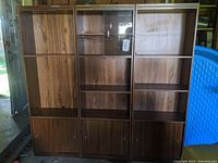 Front view of the 3 wooden bookcases showing their height, wood grain finish, closed lower cabinets, and glass doors on the middle unit.