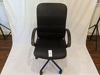 Front view of black office chair showing padded backrest, seat, armrests, and base with wheels. Visible dirt marks on seat and armrests.