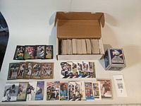 Photo showing a cardboard box filled with football cards, with some cards displayed around the box.