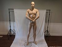 Front full body view of tall male mannequin standing on clear round stand with muscular build and neutral pose.