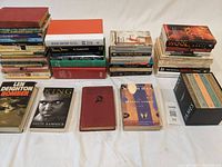 Large assortment of books stacked and laid out on a white surface showing many titles and genres