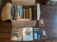 Photo showing a large box containing many DIY books including titles like 1001 Do It Yourself Hints & Tips, Concrete by Alan Ferguson, and several other books covering home and craft topics, also some manuals in slipcases.