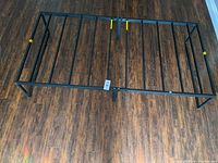 Top-side view of black metal single bed frame showing support bars and central leg on hardwood floor.