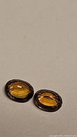 Pair of oval-shaped golden yellow faceted tourmaline gemstones placed on a flat surface.