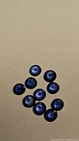 Close-up photo of ten round-cut blue sapphires on a textured beige surface showcasing color and cut.
