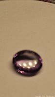 Oval cut purple amethyst gemstone shown on plain background, highlighting color and faceting.
