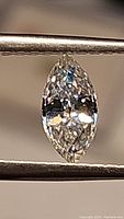 Close-up photo of the marquis cut moissanite gemstone held by tweezers showing facets and clarity.