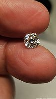Close-up image of the loose round brilliant cut moissanite gemstone held between fingers showing size and clarity.