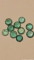 Close-up photo of ten round calibrated emerald gemstones showing deep green color and small natural inclusions.