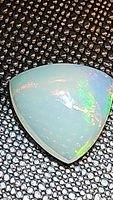 Close up photo of natural Ethiopian opal trillion cabochon showing translucent milky white body with bright internal play of colors including green, yellow and red flashes