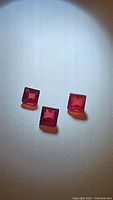 Three square cut natural rubies placed on a white surface under light, showing color and clarity.
