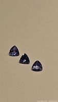 Full view of the three trillion cut natural tanzanite gemstones on a beige background.