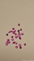 Small natural pink sapphire stones scattered on a light background, showing round cuts and bright pink color.