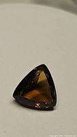 Triangular faceted natural Madeira citrine gemstone with deep cognac color shown on neutral background.