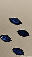 Four marquise cut sapphires arranged on a beige surface showing rich royal blue color and faceted polished surfaces.