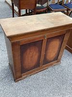 Front view of an antique wooden cabinet with a closed door showing worn wood surface and keyhole.