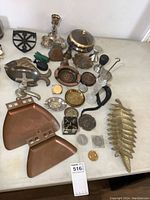 Full overview of the lot showing brass and copper items, cast iron figures, coasters, tokens, glass salt and pepper shakers and other items on a white surface.