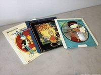 Three cartoon video disc sleeves laid flat on a surface showing artwork for Disney, Looney Tunes, and MGM titles.
