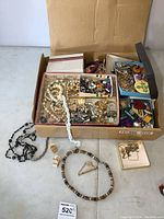 Full view of box containing multiple jewelry pieces, necklaces, pins, brooches, and some Boy Scout patches.