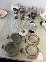 Overview of the lot showing all stoneware bowls, various glassware including stemware, decanters, and other barware on a white table