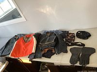 Overview photo showing multiple leather jackets, leather riding gloves, bandanas, and folded clothing items on a table.