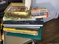Photo showing stack of books with titles visible and box of postcards on top