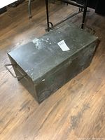 Overall view of large rectangular green metal toolbox showing surface wear and hinge on lid.