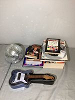 Photo showing a silver disco ball, stack of music books and magazines, and a guitar-shaped tin box.