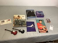 Lot items including two miniature decorative guitars, multiple music-related books, a box set of collector cards, and two postal collectible envelopes.