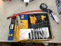Power Fist air brad nailer in original box with flexible red hose and tire pressure gauge visible on table