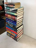 Side view of 14 stacked hardcover novels with visible titles and authors including Harlan Coben, Iris Johansen, Janet Evanovich, John Lescroart.