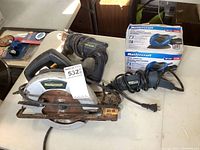 Photo showing Mastercraft circular saw, rotary tool, drill, and boxed finishing sander all placed on a white table surface.