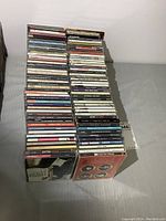 Photo showing a large stack of about 85 CDs mostly rock and roll genre stacked vertically, showing spines of cases with album and artist names.