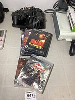 Sony PlayStation 2 console with wired controllers and game cases displayed on table with some other electronics visible nearby.