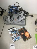 Sony PlayStation console with two wired controllers, two games, and power cables on a table surface.