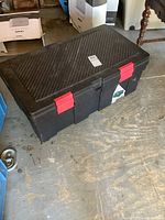 Top angle view showing textured lid with diagonal ridges and red locking latches on black resin storage bin.