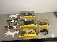 Eight toy horses displayed with four Breyer models in original yellow 'Spirit of the Horse' boxes and four loose plastic toy horses, plus a black saddle accessory.