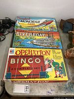 Four vintage board games stacked, showing full box covers and titles: Disneyland Monorail Game, Disneyland Riverboat Game, Operation, Bingo.