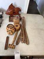 View of lot showing large carved wood fish, cylindrical coin bank, wooden gavel, folding wood ruler, three dried bean pods, wooden container and coins on table.