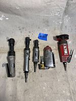 Five air tools: Four 3/8" air ratchets and one air cut off tool laid out on a surface showing wear but good condition.