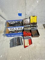 Overall view of drill bits and driver bits arranged in plastic cases and loose in cardboard boxes.