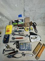 Photo of entire hand tools lot showing various wrenches, scissors, levels, measuring tape, hand planer, folding ruler and other hand tools arranged on a concrete floor.