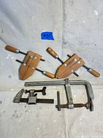Lot of 4 clamps including 2 wooden Jorgensen hand screw clamps with wooden handles, 1 large metal C-clamp, and 1 smaller metal clamp on a white cloth background.