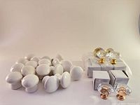 Group of white painted wooden drawer knobs and diamond-shaped crystal glass cabinet knobs in gold and rose gold-tone bases on a light background.