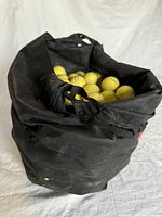 Black reusable shopping bag filled with many yellow golf balls, showing frayed handles and wear.