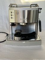Front view of the stainless steel DeLonghi espresso machine with portafilter attached, showing buttons and steam wand.
